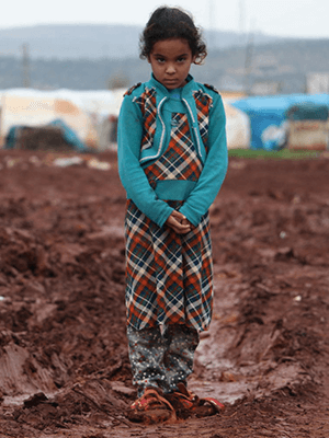 Fotografía de una niña mirando a la cámara con albergues de UNICEF al fondo