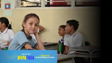 nina en pupitre de una escuela rural mirando fijamente a la camara con cara de felicidad