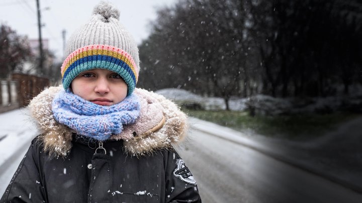 niño mirnado a la camara con cara triste en medio de una calle completamente cubierta por la nieve