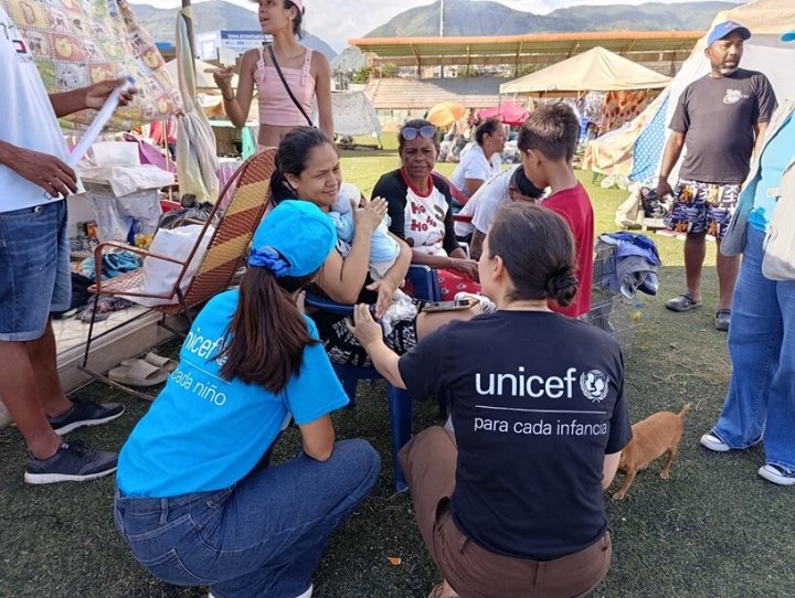funcionario de UNICEF ayudando a una mujer con un niño de brazos durante la emergencia del terremoto en venezuela