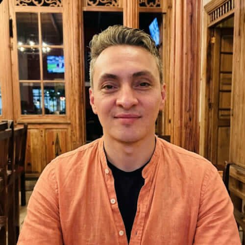 Retrato de hombre con camisa naranja sonriendo en un ambiente de madera cálida.