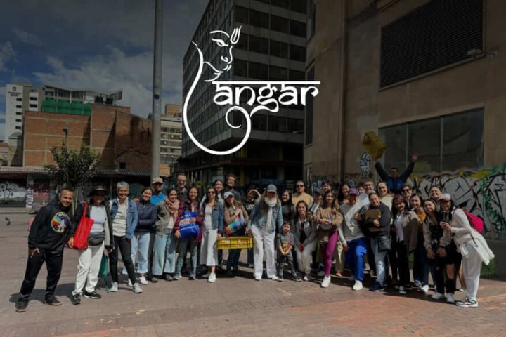 Grupo de personas posando juntas en una plaza urbana con edificios y murales de fondo, organizado por la comunidad Angar.