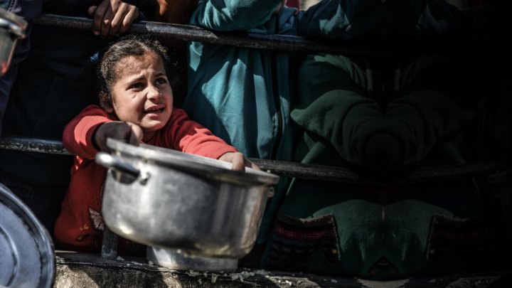 niña en gaza con desesperación pidiendo que le den comida en una olla metalica