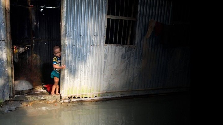 niño triste dentro de una casa de latas en medio de una inundación mirando a la camara
